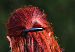 The back of a head with frizzy red hair held with a black clip.