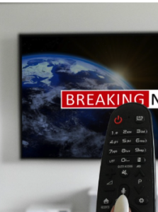 A finger on a tv remote in front of a televison playing.
